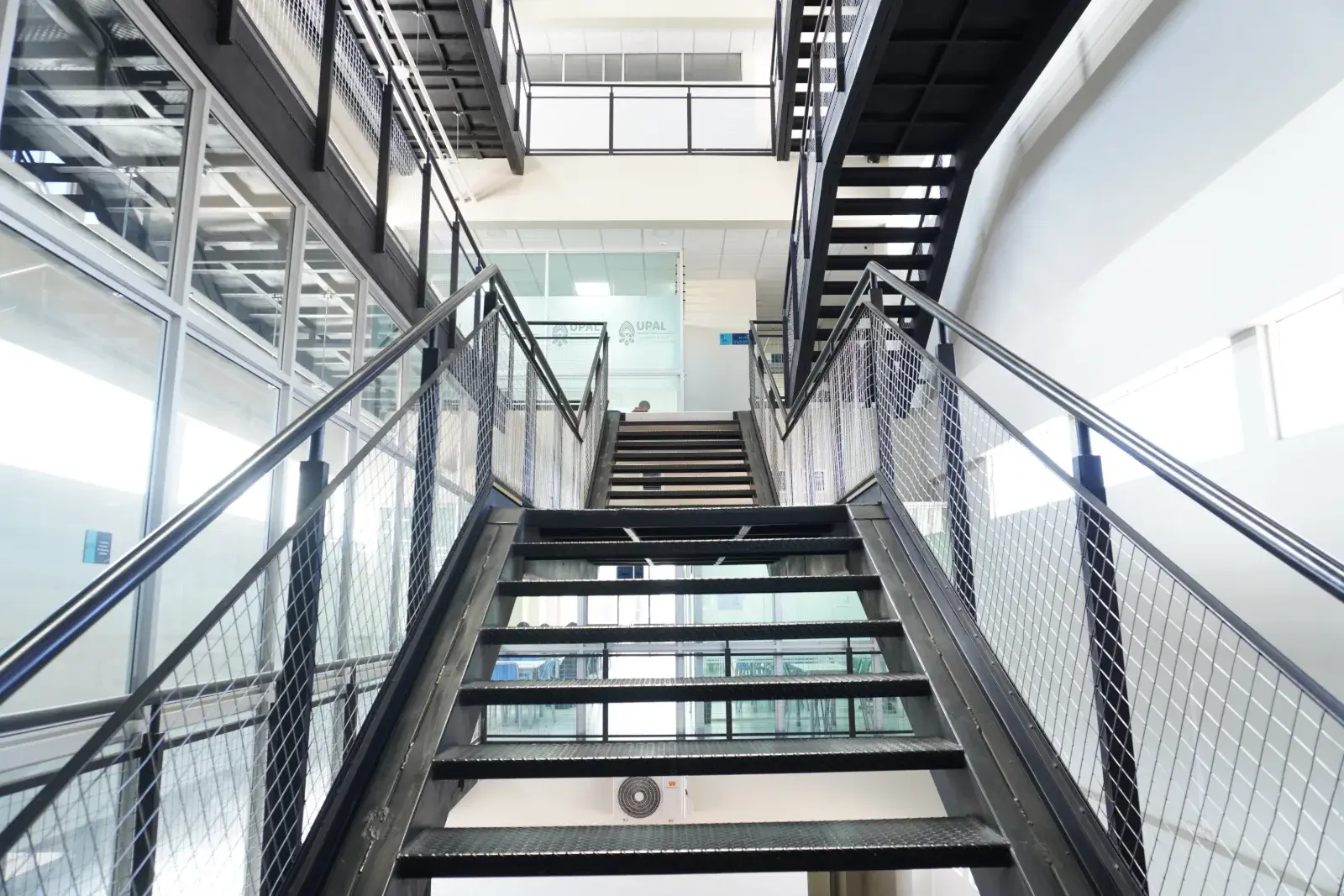 Gradas de estructura negra y vidrio en el interior del Campus Soria Galvarro