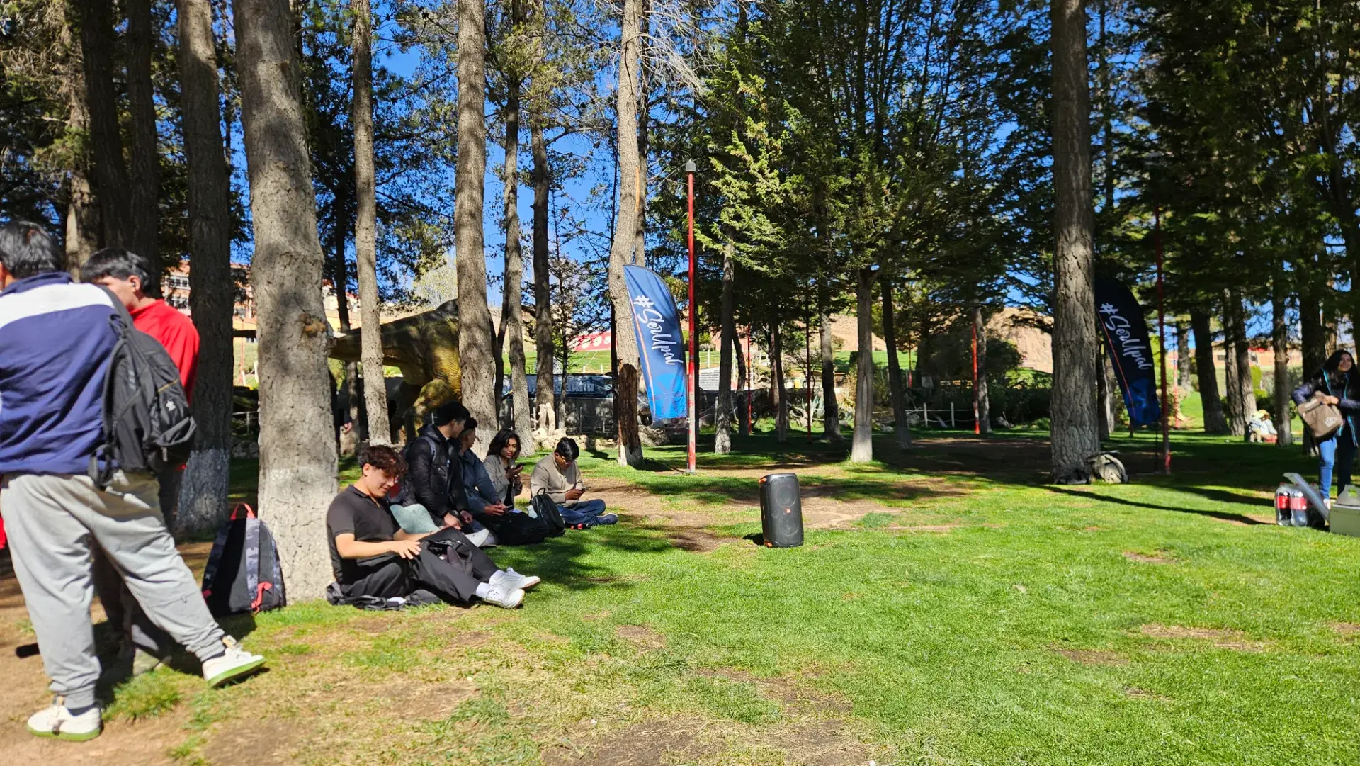 Estudiantes de la UPAL descansando bajo los árboles del campus junto a banderas #SerUpal